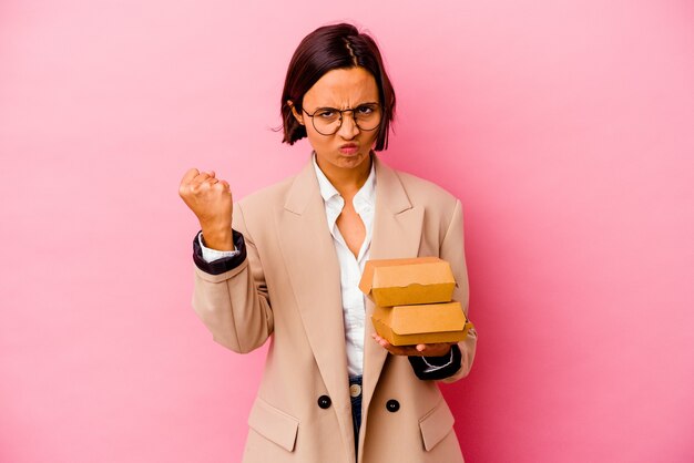 Femme de race mixte jeune entreprise isolée sur fond rose montrant le poing à la caméra, expression faciale agressive.