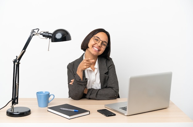 Femme de race mixte jeune entreprise travaillant au bureau pointant vers l'avant avec une expression heureuse