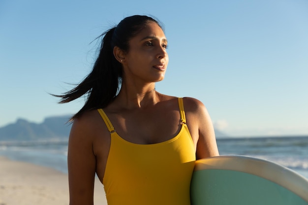 Femme de race mixte portant une planche de surf sur la plage. loisirs en plein air sains au bord de la mer.