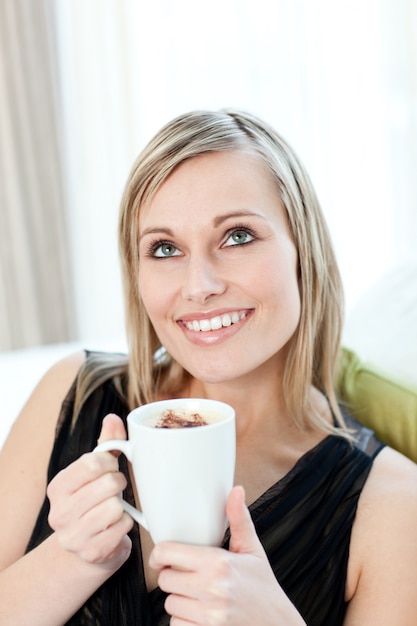 Femme radiante, boire un café assis sur un canapé