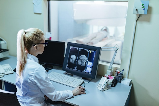 Femme radiologue supervisant la procédure d'analyse du cerveau d'un patient depuis la salle de contrôle