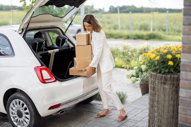 Femme ramassant un colis dans un coffre de voiture près d'une maison