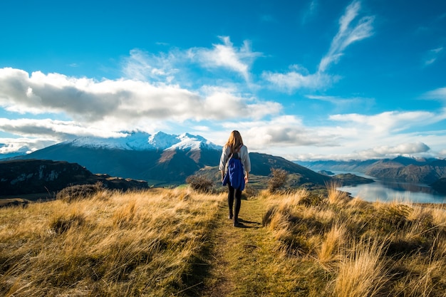 Une femme en randonnée sur l'herbe jaune sur la haute montagne. Coucher de soleil avec ciel bleu, lac et montagnes.