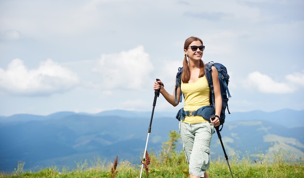 Femme, randonneur, randonnée, sur, herbe, colline, porter, sac à dos,, utilisation, bâtons trekking, dans, montagnes