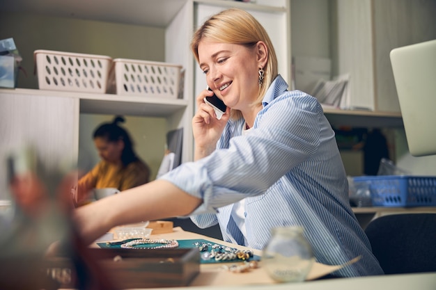 Femme ravie parlant sur smartphone pendant le processus de travail dans un studio de bijoux