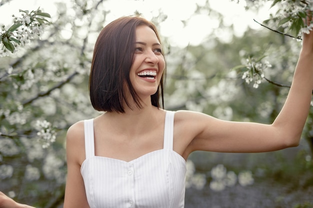 Une femme ravie de rire et de détourner les yeux tout en se tenant au milieu d'arbres en fleurs et en profitant d'une journée paisible dans un jardin de printemps