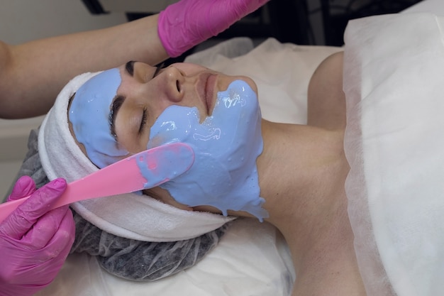 femme à la réception chez l'esthéticienne fait un masque facial alginal bleu.