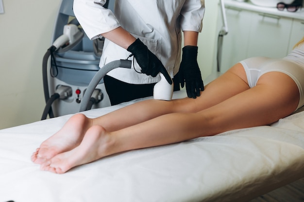 Femme recevant un traitement au laser sur ses jambes dans un salon de beauté.