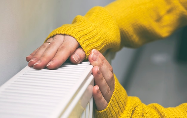 La femme réchauffe ses mains sur le radiateur