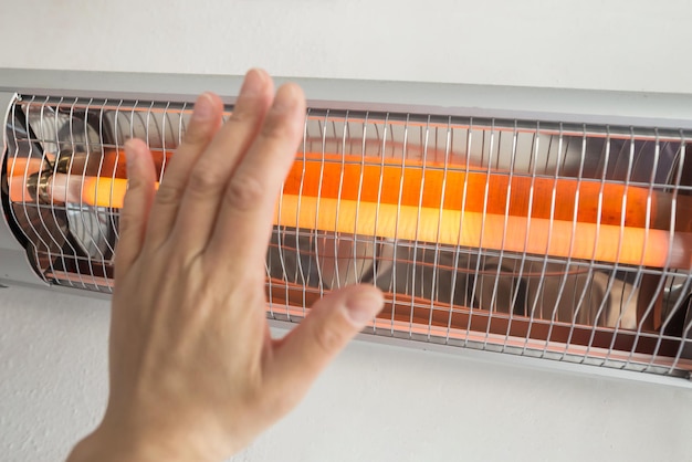 Une femme réchauffe ses paumes près d'un radiateur infrarouge électrique Gros plan