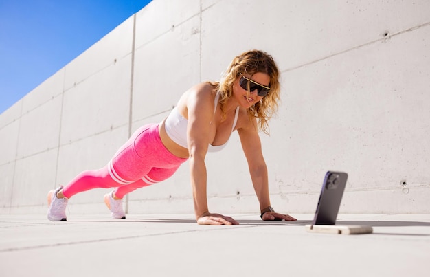 Femme à la recherche de vidéos d'exercices de fitness sur téléphone mobile pendant l'entraînement de fitness à l'extérieur