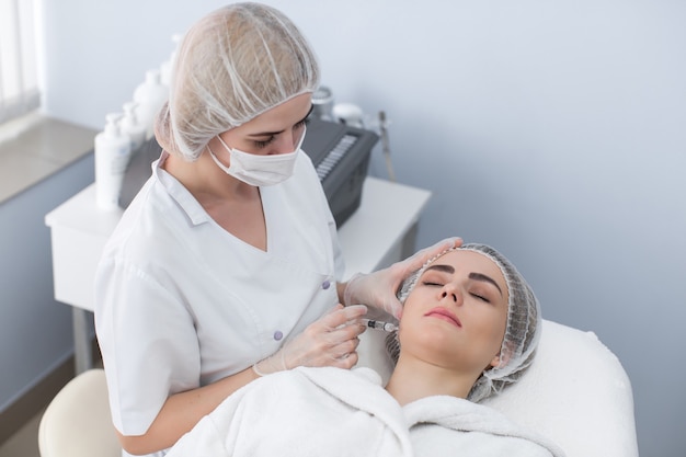 Une femme reçoit une injection dans son visage. Beauté femme donnant des injections de botox. Jeune femme reçoit des injections faciales de beauté dans le salon de cosmétologie. Injection de vieillissement du visage. Médecine esthétique, cosmétologie