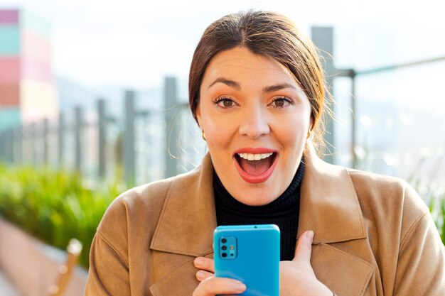 Une femme reçoit de très bonnes nouvelles tout en tenant un téléphone portable regarde directement avec une expression heureuse