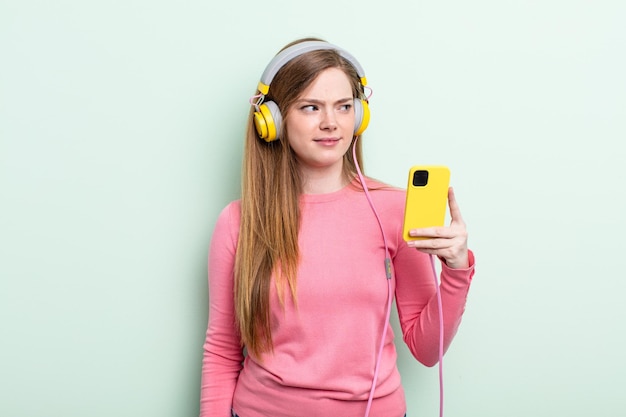 Femme Redhair se sentant triste bouleversée ou en colère et regardant sur le côté des écouteurs et du concept de smartphone