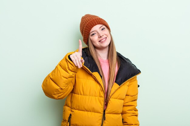 Femme Redhair souriant fièrement et en toute confiance faisant le numéro un. notion d'hiver