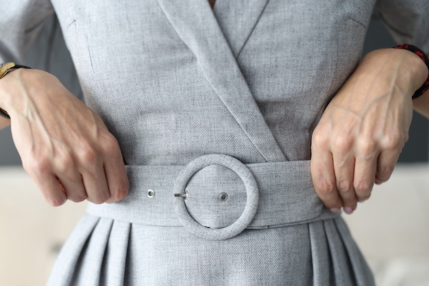 Photo femme redressant sa ceinture sur une robe grise avec ses mains en gros plan essayant des vêtements pour la maison