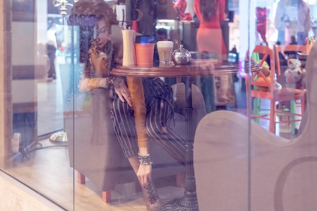 femme redresse ses chaussures tout en étant assis à une table dans un café derrière une vitre