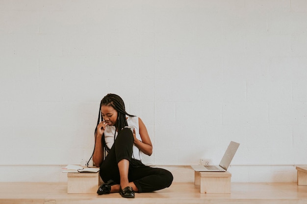 Femme réfléchie assise sur un plancher en bois et regardant son agenda