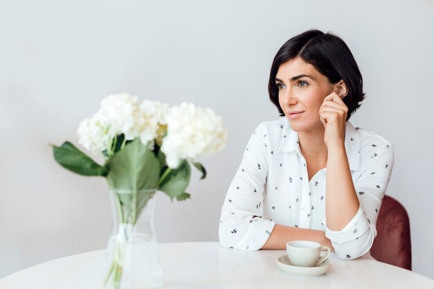 Femme réfléchie assise avec une tasse de café