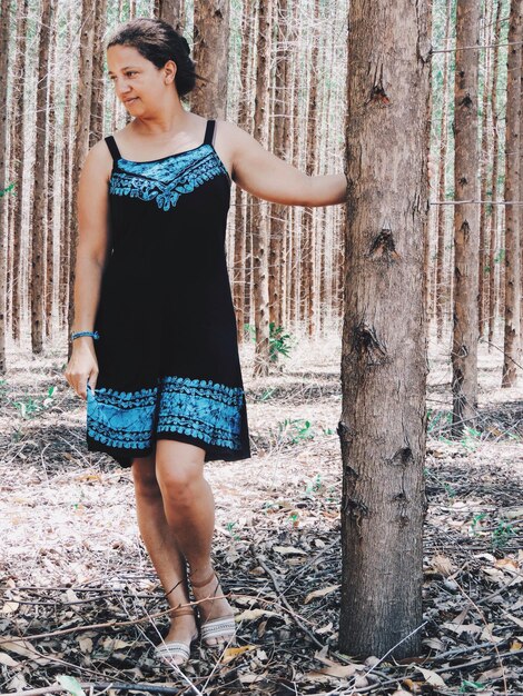 Photo une femme réfléchie debout près d'un tronc d'arbre dans la forêt