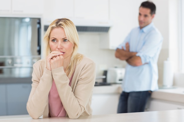 Femme réfléchie avec un homme flou en arrière-plan dans la cuisine