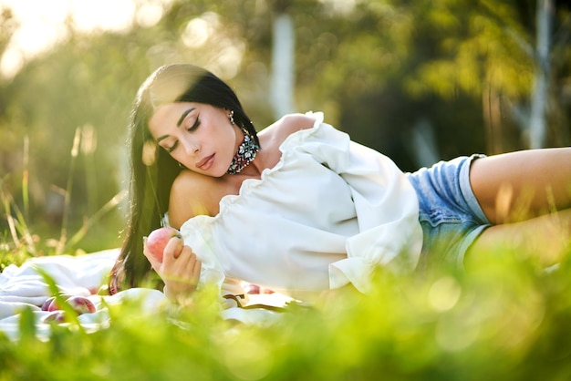 Femme réfléchie avec une pomme récoltée reposant sur un tapis de pique-nique par une journée ensoleillée.