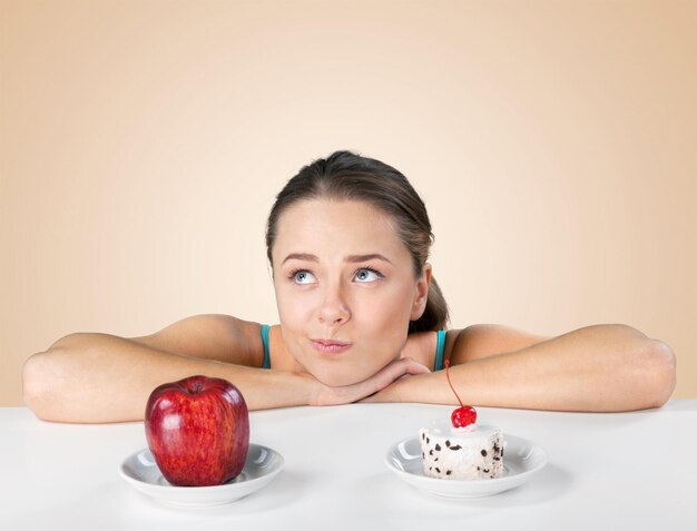 Femme réfléchie prenant la décision entre la pomme et le gâteau