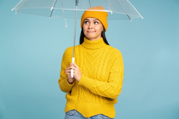 Une femme réfléchie regarde l'espace vide pour votre annonce, publicité. Personne de sexe féminin tenant un parapluie de pluie debout au mur de texture isolé en studio