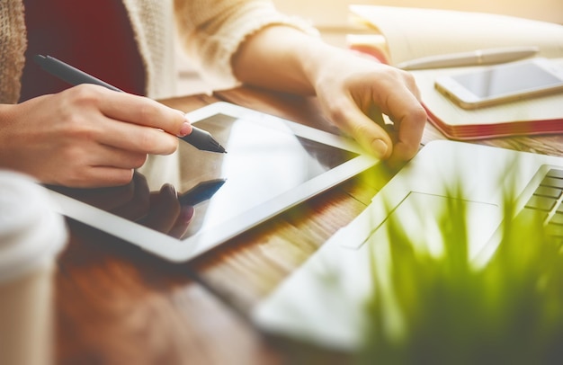 Une femme réfléchie travaillant avec une tablette et un ordinateur portable alors qu'elle était assise au bureau.