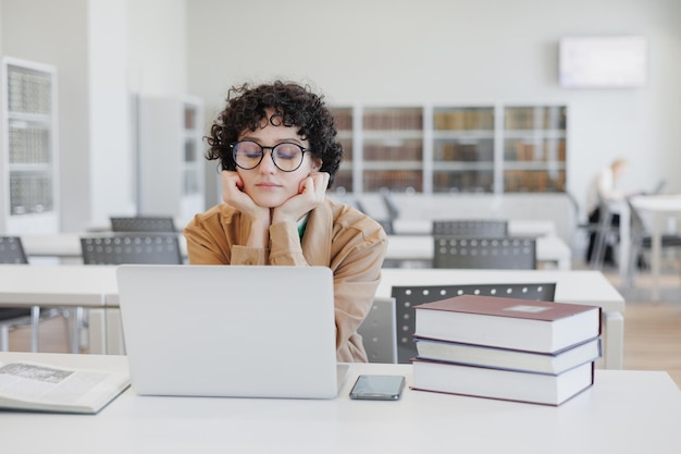 Une femme réfléchie travaille dans une bibliothèque regarde un webinaire éducatif sur Internet s'ennuie de coworking derrière un ordinateur portable