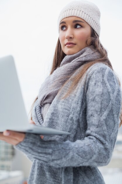 Femme réfléchie avec des vêtements d&#39;hiver en utilisant son ordinateur portable