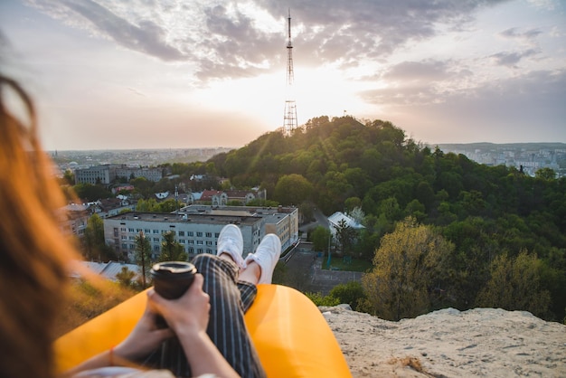 Femme regardant le coucher du soleil sur la ville en buvant du café