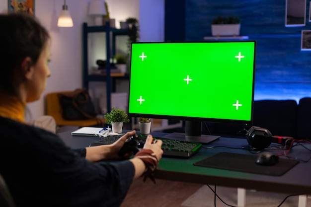 Femme regardant un écran vert horizontal sur un moniteur, jouant à des jeux vidéo avec une manette. Joueur utilisant une clé chroma avec un arrière-plan isolé et un modèle de maquette sur l'écran de l'ordinateur.