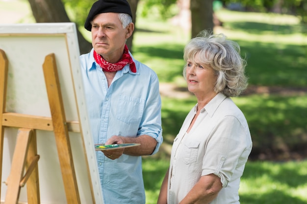Femme regardant un homme mûr peindre dans le parc