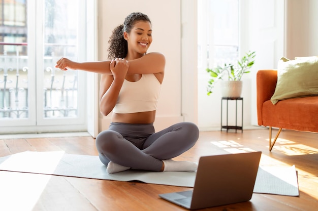 Femme regardant un ordinateur portable pendant un entraînement en ligne étirant le bras à l'intérieur