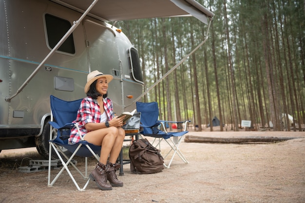 Femme regardant un ordinateur portable près du camping. vacances en caravane. voyage de vacances en famille, voyage de vacances en camping-car. femme lisant un livre dans le coffre de la voiture. apprentissage féminin sur les pauses de voyage, pose