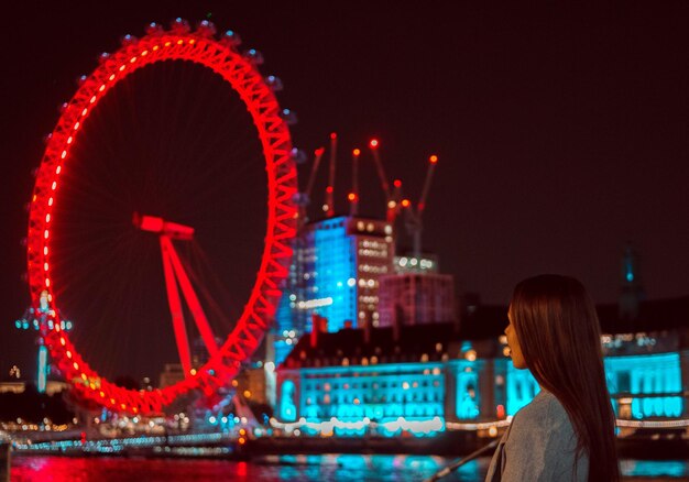 Photo une femme regardant une roue en ferris illuminée contre le ciel la nuit