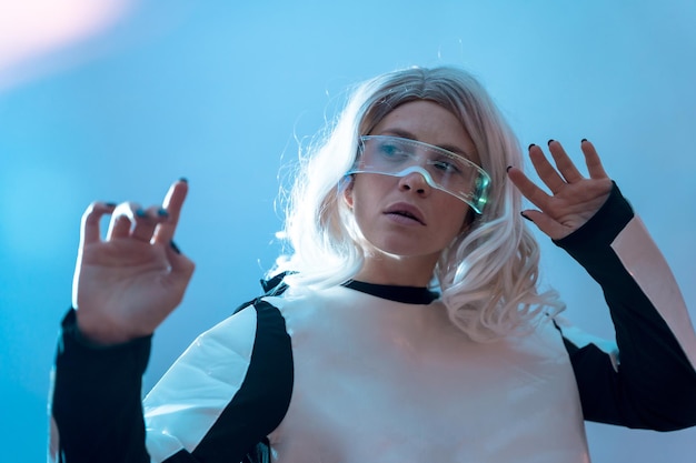 Femme regardant à travers les lunettes futuristes illuminées de réalité virtuelle sur fond bleu