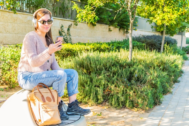 Femme regardant des vidéos dans un téléphone intelligent avec des écouteurs assis dans un parc