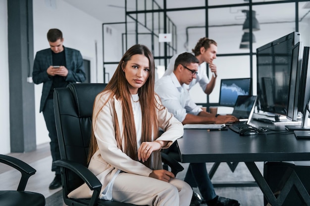 Femme regarde dans la caméra L'équipe de courtiers en valeurs mobilières travaille dans un bureau moderne avec de nombreux écrans d'affichage