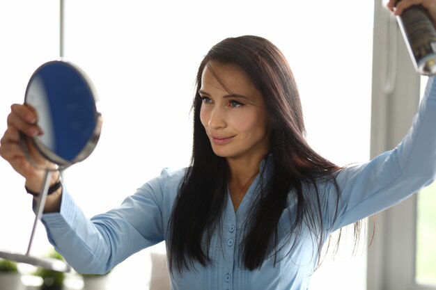 Femme regarde dans le miroir et répare ses cheveux avec du vernis