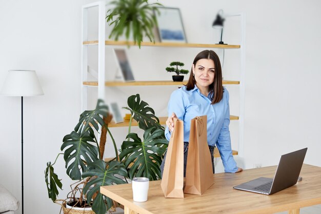 Une femme regarde dans des sacs en papier et compare ses achats avec son ordinateur portable