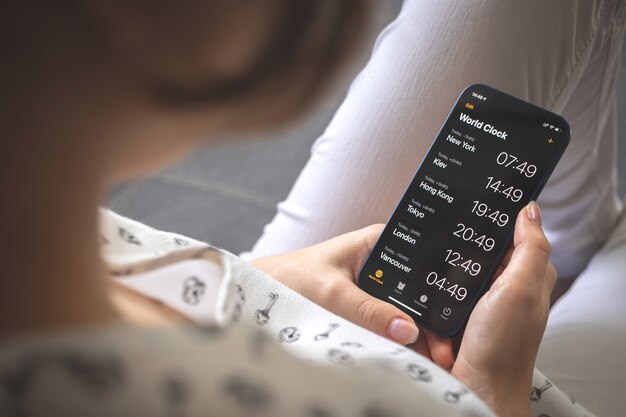 La femme regarde l'écran de l'horloge mondiale sur son téléphone portable. Écran de smartphone avec l'heure du globe, photo de concept d'entreprise