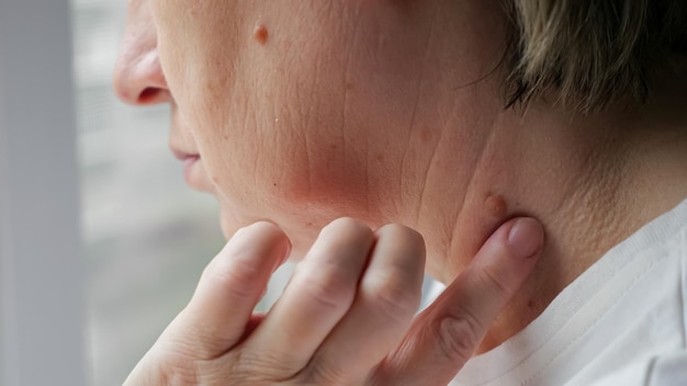 Une femme regarde par la fenêtre et touche un point douloureux sur le cou