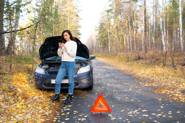 Une femme regarde sous le capot une femme répare une panne de voiture