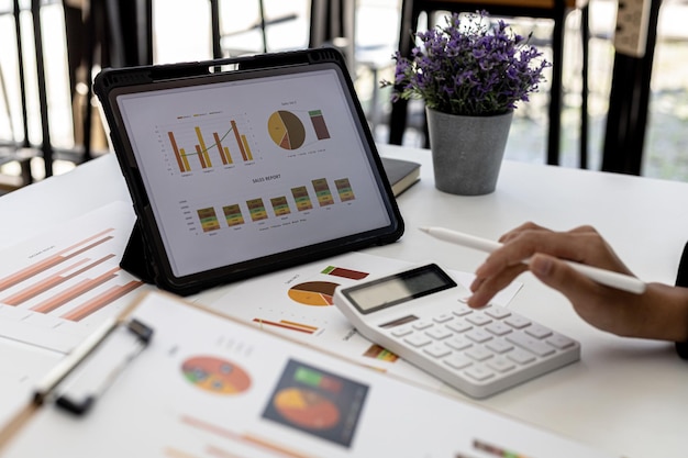 Une femme regarde une tablette sur un écran affichant le tableau de la situation financière de l'entreprise et appuie sur une calculatrice pour vérifier, un employé des finances vérifie les documents. Concept de gestion financière de l'entreprise.