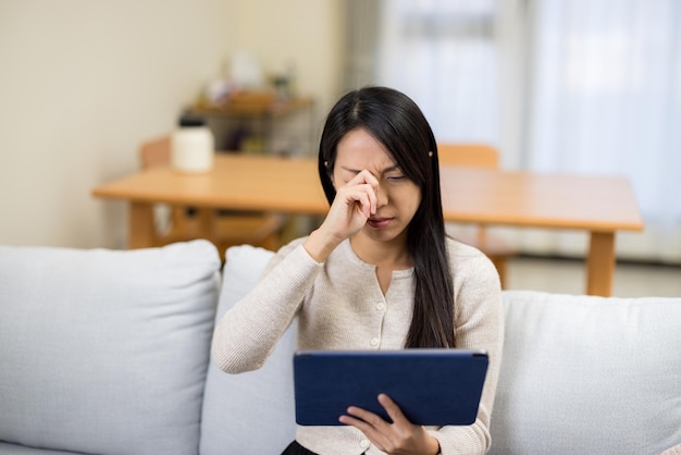 Une femme regarde une tablette numérique et se frotte les yeux.