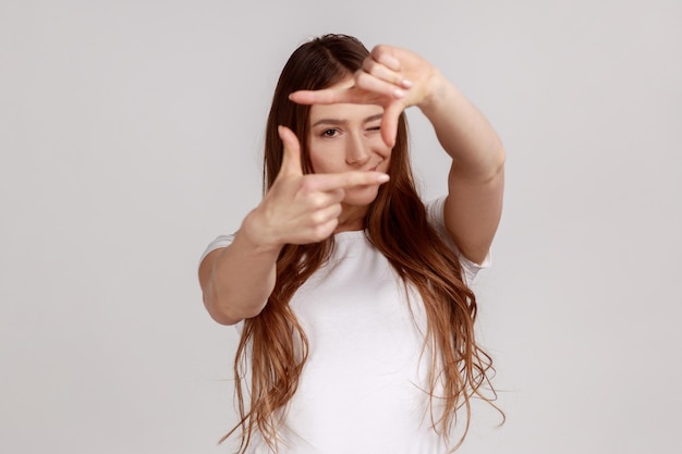 Une femme regarde à travers le cadre du doigt en imitant de prendre une photo en se concentrant et en recadrant un moment intéressant