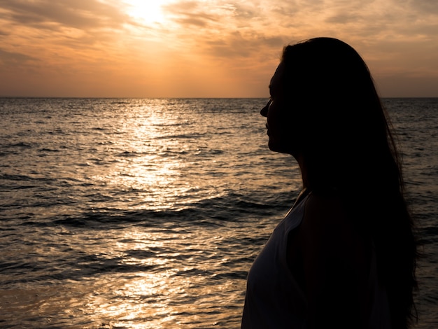 Femme relaxante à la plage pendant le beau coucher de soleil. Vacances détente humaine