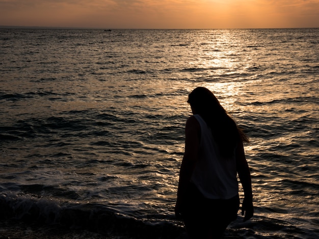 Femme relaxante à la plage pendant le beau coucher de soleil. Vacances détente humaine